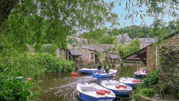 Un canal bordé de bateaux amarrés le long des rives, entouré de verdure et de bâtiments historiques.