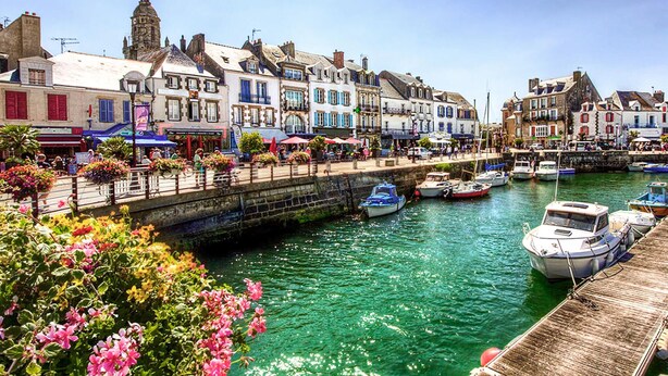 Un paseo marítimo con edificios históricos, un canal con barcos y un muelle de madera.
