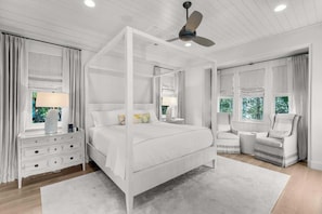 A bedroom with a four-poster bed, a nightstand with drawers, a chair, and a ceiling fan.