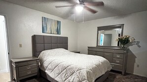 A bedroom with a bed, nightstands, a dresser, a ceiling fan, a painting, and a mirror. - Beautiful Alaskan 2 Bedroom (Anchorage)