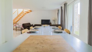 A dining area with a long table set for four, a sofa, a TV, and a lamp. - Beautiful home in Monthenault with WiFi (Monthenault)