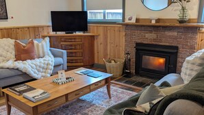 A cozy living room with a fireplace, a television, a coffee table with books, and a comfortable sofa.