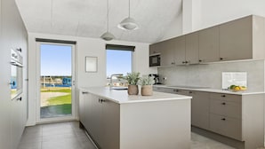 A modern kitchen with a large island, built-in appliances, and a view to a backyard. - Cozy home in Bogense with sauna (Bogense)