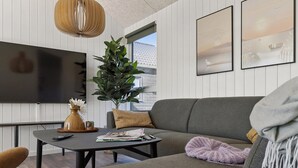 A modern living room with a grey sofa, a black coffee table, a large TV, and a potted plant. - Cozy home in Bogense with sauna (Bogense)