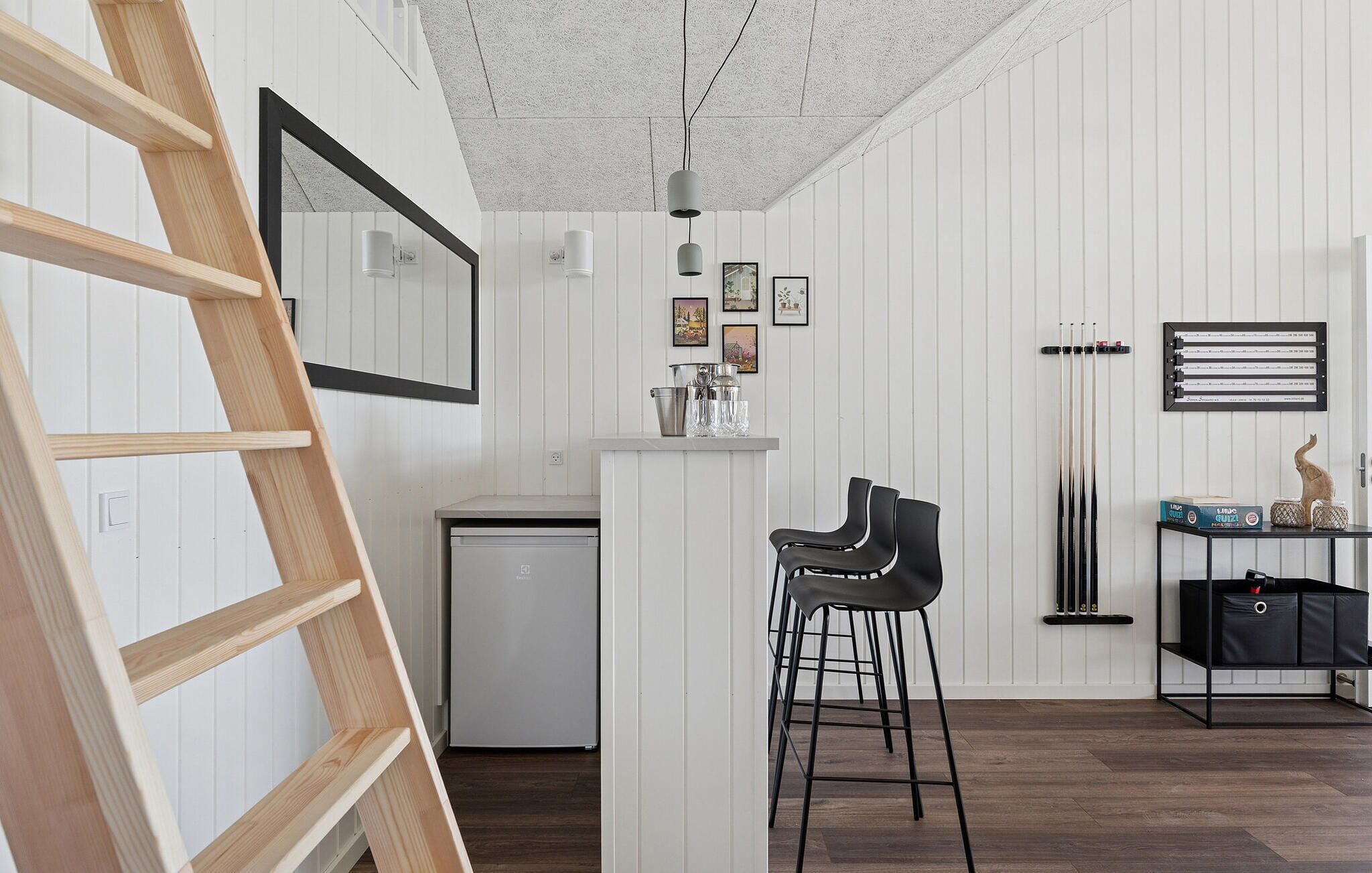 A compact kitchen with a white fridge, a bar area with stools, and a wooden ladder.