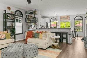 A modern living room with a sofa, ottomans, and a dining area with a kitchen in the background. - The BlueGrasshopper South Haven (South Haven)
