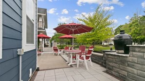 En udendørs patio med røde stole og parasoller, en stenvæg og en grill.