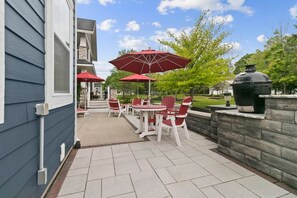 Eine Terrasse im Freien mit roten Stühlen und Sonnenschirmen, einer Steinsäule und einem Grill.