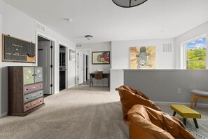 A spacious room with a large window, a brown leather sofa, a small yellow stool, and a wooden cabinet with drawers. - The BlueGrasshopper South Haven (South Haven)