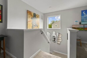A staircase with a white railing, a window with a view of a house, and a wall with abstract art.