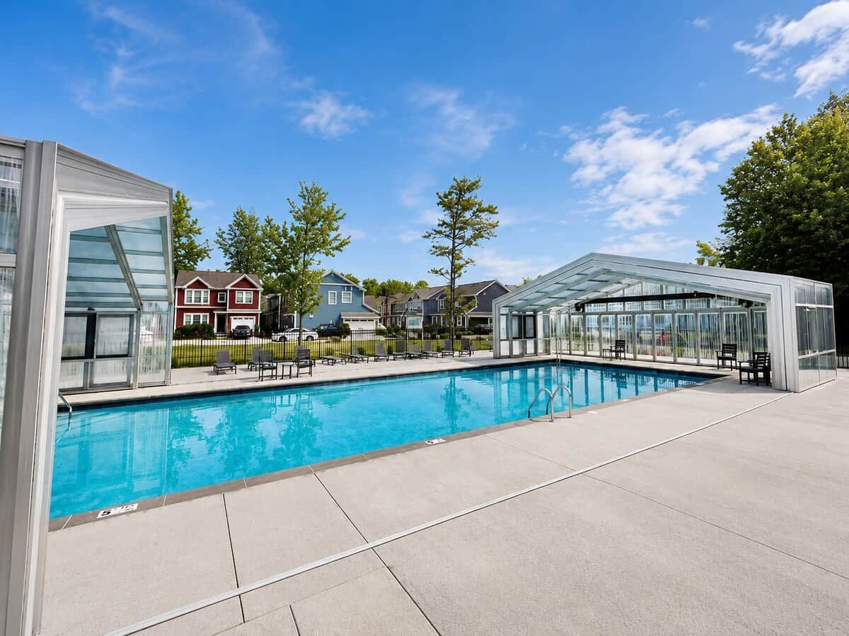 A swimming pool with a glass enclosure, a covered seating area, and houses in the background.