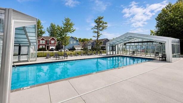 En swimmingpool med et glaslaug, et overdækket opholdsområde og huse i baggrunden.