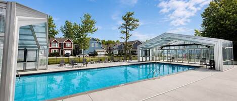 A swimming pool with a glass enclosure, a covered seating area, and houses in the background.