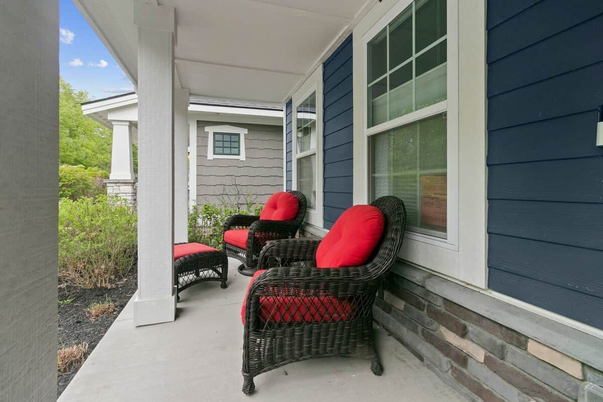 A porch with wicker chairs and red cushions, a stone wall, and a blue house exterior.