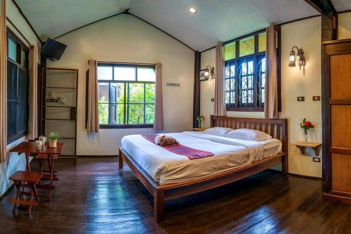 A room with a wooden bed, a small table with a plant, a cabinet, and a window with curtains.