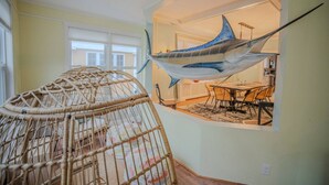 A room with a large fish sculpture hanging from the ceiling, a wicker chair, and a dining area with a table and chairs. - Luxury 6BR Beach Home, Sleeps 16  – 1.5 Blks to Beach (Atlantic City)