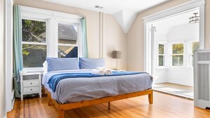 A bedroom with a wooden bed, a nightstand, a lamp, and large windows. - Luxury 6BR Beach Home, Sleeps 16  – 1.5 Blks to Beach (Atlantic City)
