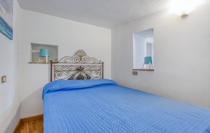 Un dormitorio con una cama, un espejo en la pared y una estantería con una lámpara.