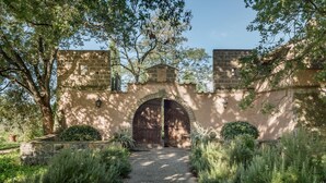 A stone archway leading to a building with a brick facade, surrounded by greenery and trees.