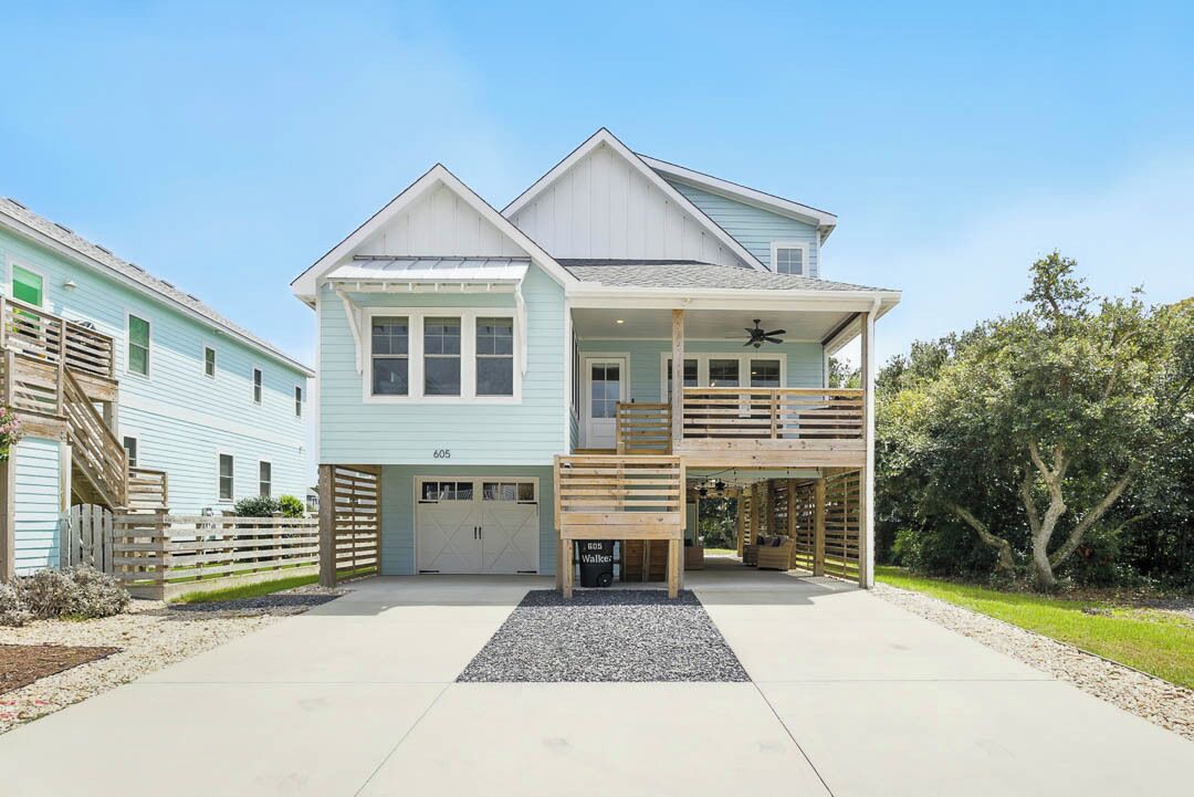 Ein zweistöckiges Haus mit einer überdachten Veranda, einer Garage und einer kleinen Terrasse.