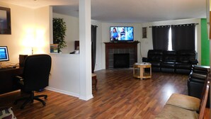 Un salon avec une cheminée, un téléviseur, un bureau avec un ordinateur et un canapé en cuir noir.