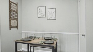 Un comedor con una mesa de madera dispuesta para cuatro personas, un banco y dos láminas botánicas enmarcadas en la pared.