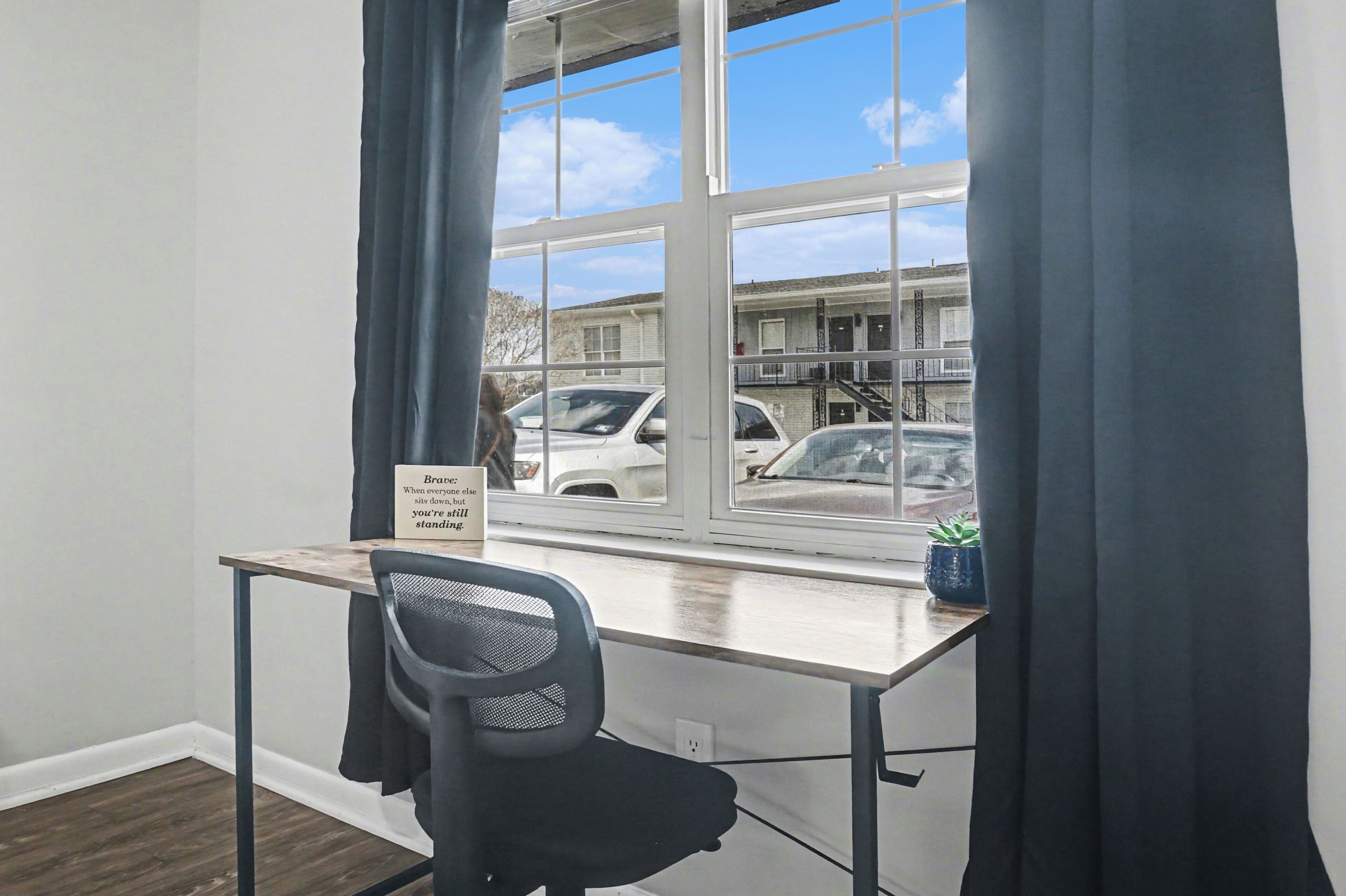 A room with a desk, chair, window, and curtains.