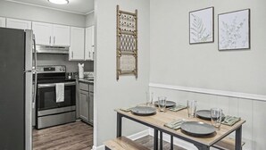 Una cocina moderna con armarios blancos, un refrigerador de acero inoxidable y una mesa de comedor de madera con platos y vasos.