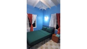 Una stanza con un letto singolo, un comodino, una finestra con tende e una ventola a soffitto.