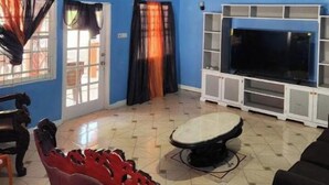 Un soggiorno con una parete blu, una TV su un mobile bianco, una poltrona rossa e un ventilatore a soffitto.