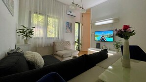 A modern living room with a sofa, a coffee table, a TV, and a potted plant.