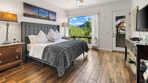 Un dormitorio con una cama grande, un ventilador de techo y vistas a la vegetación a través de un ventanal.
