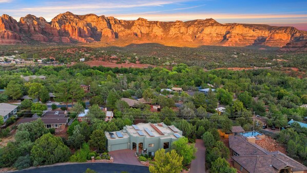 A residential area with houses surrounded by dense greenery and mountains in the background.