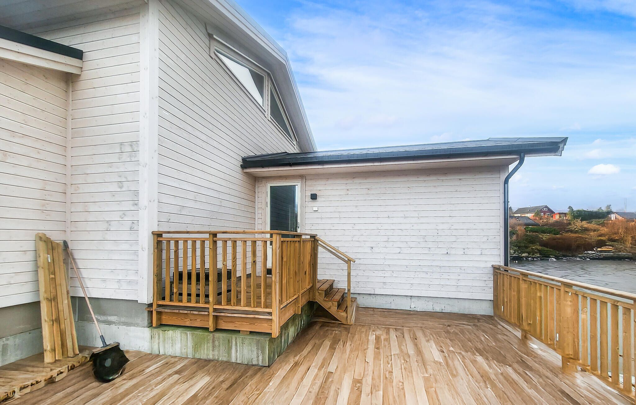 A wooden deck with a wooden railing, a door, and a view of a river and distant buildings.