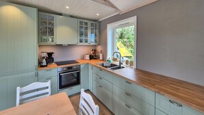 Une cuisine avec des meubles de couleur vert clair, un plan de travail en bois, un four encastré et une fenêtre donnant sur un paysage verdoyant.