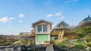 Une maison située sur la côte, dotée d’une structure centrale, d’une terrasse en bois et d’un escalier menant à un deuxième étage.