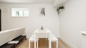 A minimalist living room with a white sofa, a white table with a plant, a framed artwork, and a window with a view. - Cozy & Spacious 2BR Guest Suite, Near Vancouver (Langley Township)