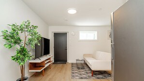 A modern living room with a flat-screen TV, a white sofa, a small coffee table, and a potted plant. - Cozy & Spacious 2BR Guest Suite, Near Vancouver (Langley Township)