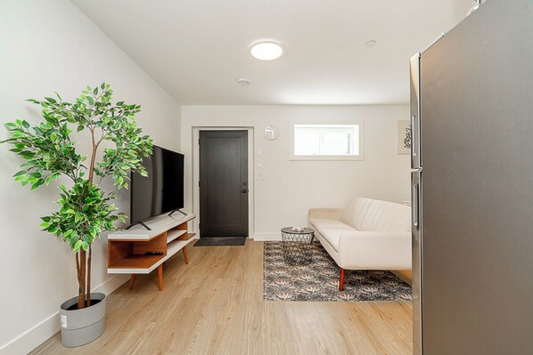 A modern living room with a flat-screen TV, a white sofa, a small coffee table, and a potted plant. - Cozy & Spacious 2BR Guest Suite, Near Vancouver (Langley Township)