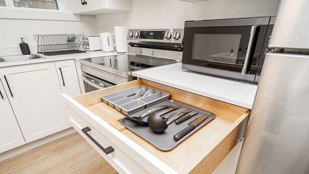 A modern kitchen with white cabinets, stainless steel appliances, and a wooden countertop with a cutting board and utensils. - Cozy & Spacious 2BR Guest Suite, Near Vancouver (Langley Township)