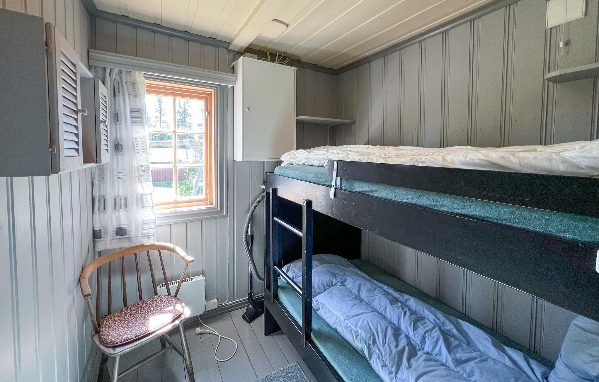 A bunk bed room with a window, a chair, and a radiator.