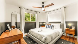 A modern bedroom with a large bed, a desk, a chair, a nightstand, a ceiling fan, and a window with curtains. - Modern Retreat w/ Hot Tub, Peloton, Gym, and BBQ (Westminster)