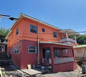 Um edifício de dois andares com fachada vermelha, uma varanda no andar superior e materiais de construção no chão.