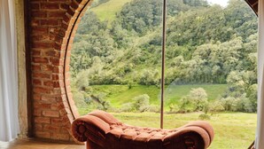 Une pièce avec un mur en briques, une grande fenêtre et un fauteuil marron avec des coussins.