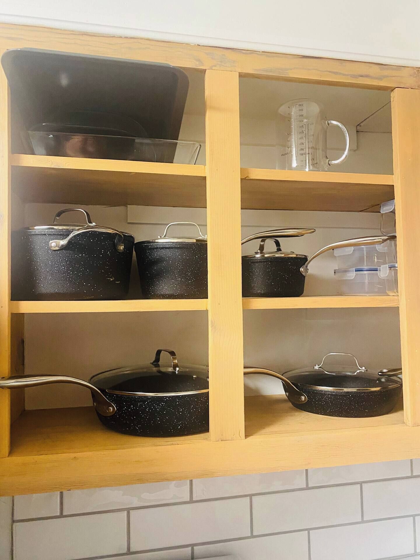 A kitchen cabinet with multiple shelves, each holding various kitchenware items like pots and pans.