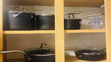 A kitchen cabinet with multiple shelves, each holding various kitchenware items like pots and pans.