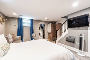 A bedroom with a large bed, a TV mounted on the wall, a heater, and a staircase leading to another room. - Entire DC Home + Private Suite Near Metro (Washington)