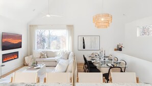 A modern living room with a fireplace, a sofa, a dining table with chairs, and artwork on the walls. - Pool + Hot Tub + Plunge | Scandinavian Wellness Retreat (Weaverville)