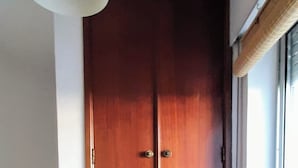 A room with a wooden wardrobe, a hanging light fixture, a window with a blind, and a striped rug on the floor. - 2-bedr. house in the tranquillity of Azeitão. (Vendas de Azeitão)