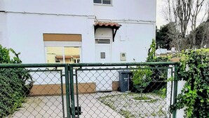 A two-story building with a white facade and brown roof tiles. There is a chain-link fence in front of the building. - 2-bedr. house in the tranquillity of Azeitão. (Vendas de Azeitão)
